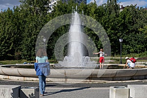 Mother with teen girl and boy having fun on fountain at sunny summer park. family walk, leisure