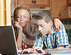 Mother and teen son work in kitchen on laptop photo