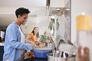 Mother With Teenage Daughter Helping To Prepare Meal At Home In Kitchen Together