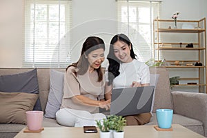 Mother and teenage daughter are looking at social media on laptop together on the sofa in the living room.