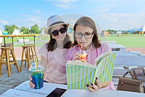 Mother and teenage daughter in outdoor cafe with soft drinks reading book