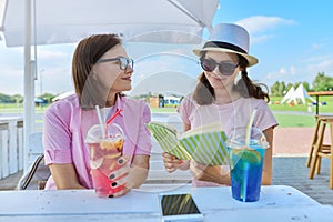 Mother and teenage daughter in outdoor cafe with soft drinks reading book