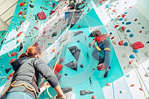 Mother and teenage son at indoor climbing wall gym. Boy using a top rope belay with climbing harness and mom belaying him on the