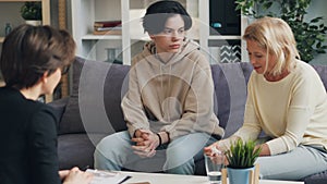 Mother and teenage son talking to psychologist in office hugging and smiling