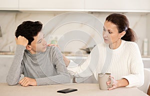 Mother and teenager son drink tea and talk while sitting in kitchen