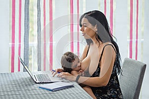 Mother teleworking in the dining room while breastfeeding