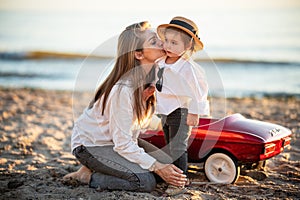 Mother tenderly kissing small daughter in hat having fun together on sea beach.