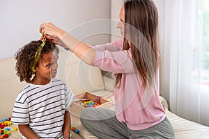 A mother tenderly ties her mixed-race confused daughters hair, both smiling, in a cozy, sunlit room moment of maternal