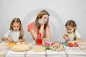 Mother with tenderness looks like her little daughter to help her in kitchen to prepare meals