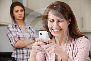 Mother Texts On Mobile Phone As Daughter Watches In Background