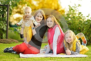Mother and three children having fun on autumn day in city park. Adorable baby boy being held by his mommy. Two older sisters