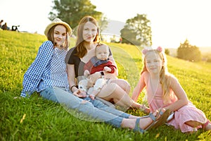 Mother and three children having fun on summer day in city park. Adorable baby boy being held by his mommy. Two older sisters