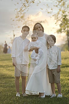 Mother and three children hugging. Happy family sitting outdoor: woman and two brother kids boys and cute little toddler