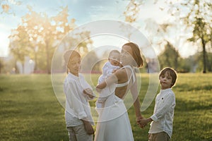 Mother and three children hugging. Happy family sitting outdoor: woman and two brother kids boys and cute little toddler