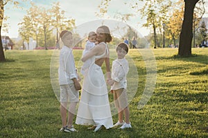 Mother and three children hugging. Happy family sitting outdoor: woman and two brother kids boys and cute little toddler