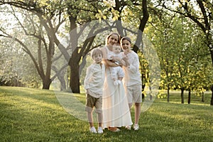 Mother and three children hugging. Happy family sitting outdoor: woman and two brother kids boys and cute little toddler