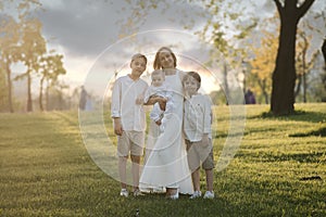 Mother and three children hugging. Happy family sitting outdoor: woman and two brother kids boys and cute little toddler