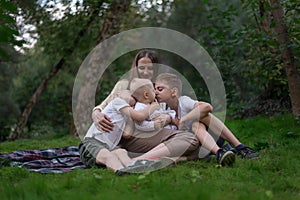 Mother and three children sitting on picnic blanket in park. Happy friendly family. Two brothers hug little sister