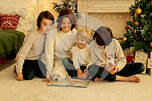 Mother with three kids and dog, sitting at home at Christmas, cozy atmosphere, Christmas time reading book