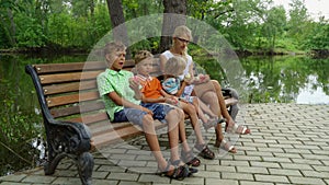 Mother with three kids sitting on the bench and eating apples