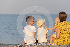 Mother and three small children sitting on the beach on sea background. Summer vacation with family