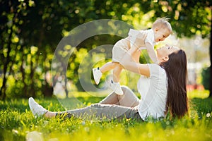 Mother throws baby up, playing and laughing in sun summer day on nature. Happy family outdoors