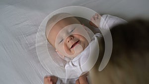 Mother tickles the baby and he laughs lying on the bed