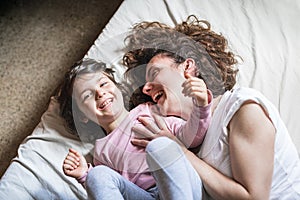 Mother tickles her laughing daughter on the bed