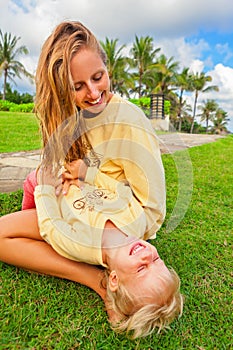 Mother tickling funny baby son lying on her laps