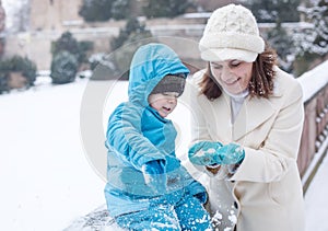 Mother and toddler boy having fun with snow on winter day