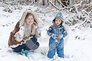 Mother and toddler boy having fun with snow on winter day