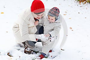 Mother and toddler boy having fun with snow on winter day