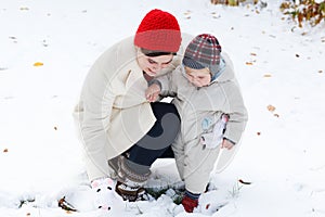 Mother and toddler boy having fun with snow on winter day