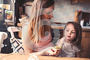 Mother and toddler daughter eating grapes for breakfast at home