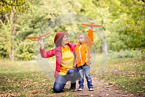 Mother and toddler son launching toy aircrafts in autumn park. Mom is kneeling, embracing her child. Dreams and travel concept