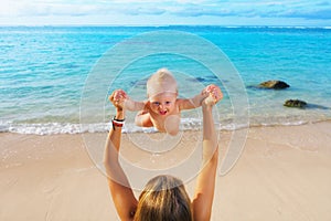 Mother tossing to mid air happy baby on sea beach