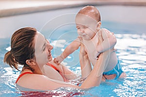 Mother traning her newborn baby to float in swimming pool photo