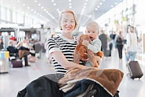 Mother traveling with child, holding his infant baby boy at airport terminal waiting to board a plane. Travel with kids