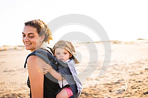 Mother turning to see the baby that holds on her back in a baby carrier outdoors