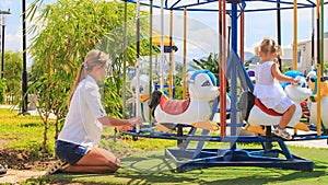 mother turns fast two girls with hairtails on merry-go-round