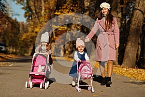 Mother and two baby daughters with stroller walking on autumn park