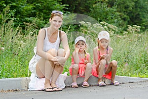 Mother and two children sitting on curb of the road waiting for the bus