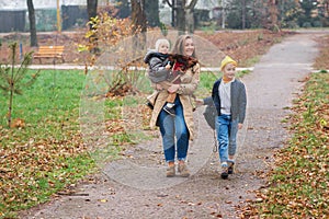 Mother and two children walking in autumn park. Happy family enjoying beautiful autumn nature. Cool autumn weather. Stylish young