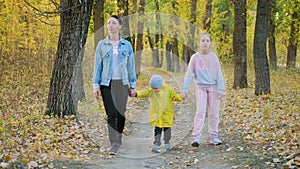 Mother and two children walking in the park and enjoying the beautiful autumn nature. Happy family on autumn walk.