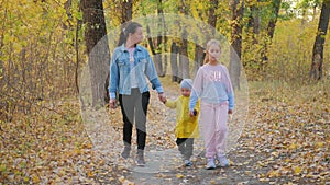 Mother and two children walking in the park and enjoying the beautiful autumn nature. Happy family on autumn walk.