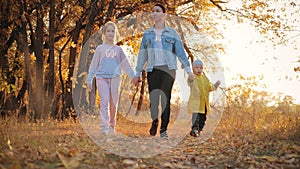 Mother and two children walking in the park and enjoying the beautiful autumn nature. Happy family on autumn walk.