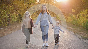 Mother and two children walking in the park and enjoying the beautiful autumn nature. Happy family on autumn walk.