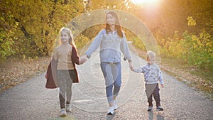 Mother and two children walking in the park and enjoying the beautiful autumn nature. Happy family on autumn walk.