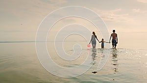 Mother and two children walking on the shallow water at sunset