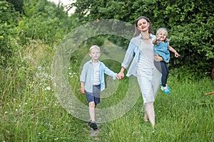 Mother with two children walks in nature. Little brother and sister. Summer clothes. Family time